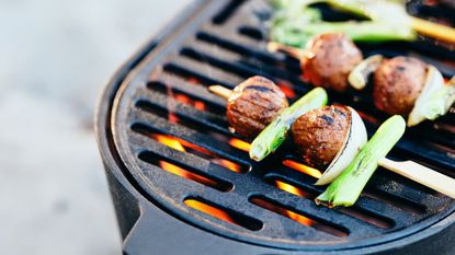 A close up of meatballs and vegetables on wooden sticks on a cast iron barbeque grill 