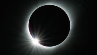 total solar eclipse with a burst of sunlight emerging from behind the moon in the lower left corner. 