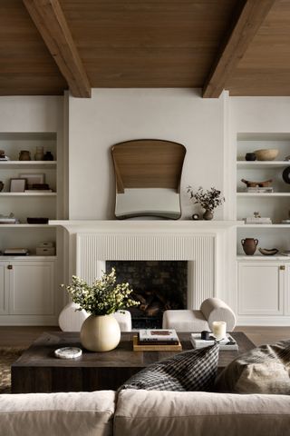 A living room with a wooden ceiling, and a mantel with a mirror placed atop