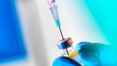 A syringe is shown being inserted into a vaccine vial. 