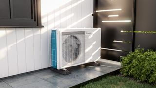 air source heat pump on paved path outside home with black fence panels next to it with gaps where sunlight filters through