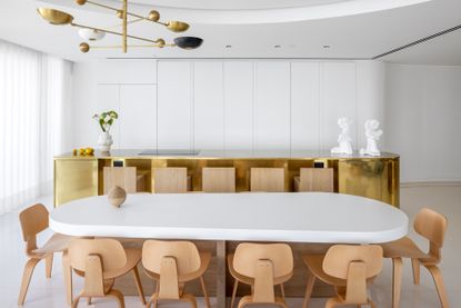 dining area at Tel Aviv apartment by Alex Meitlis with large white table with wooden chairs and a gold kitchen island