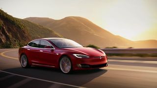 Une Tesla Model S roulant sur une route de montagne au coucher du soleil.