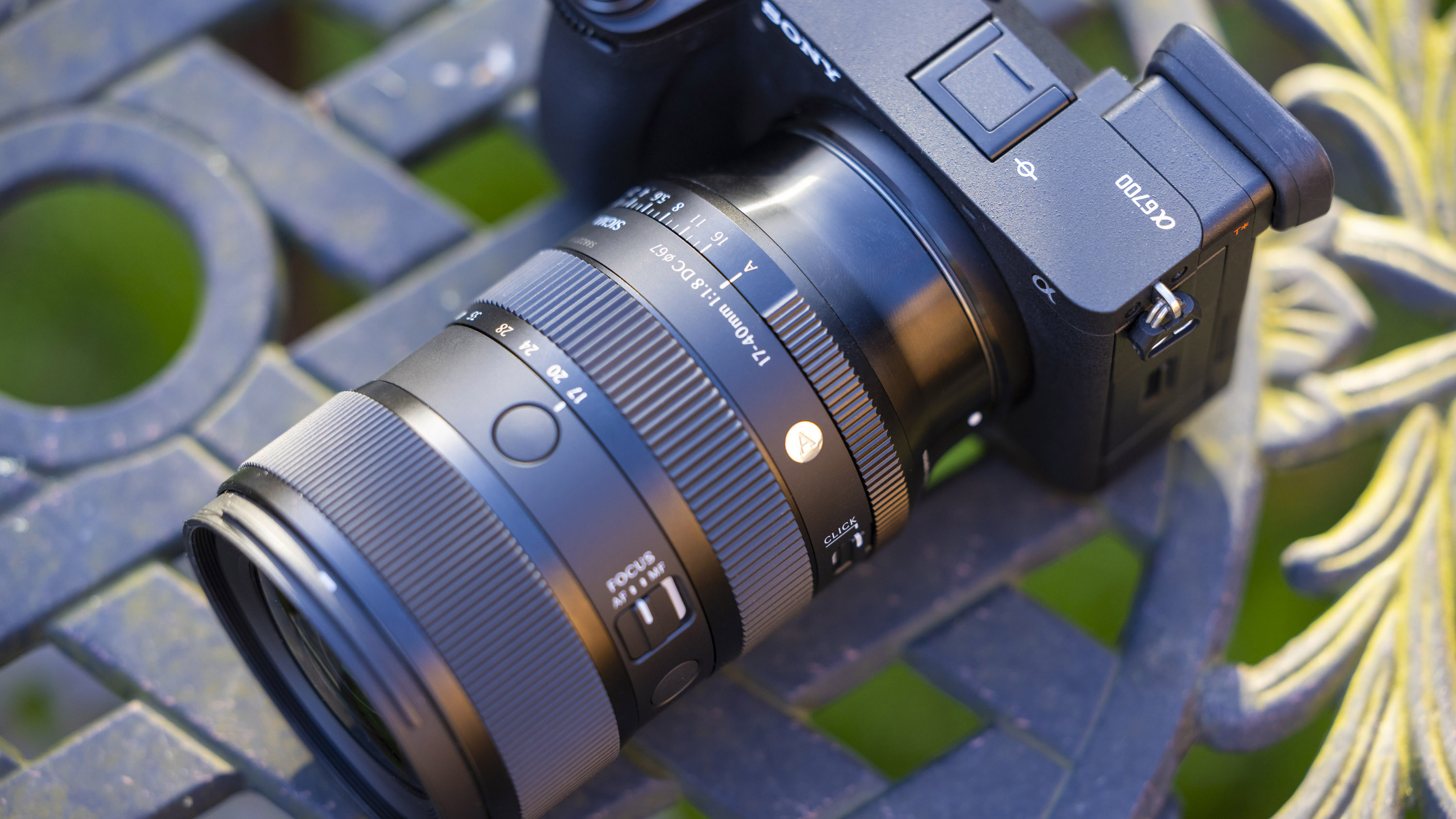 Sigma 17-40mm f1.8 DC Art lens product shot taken outdoors on a metal garden table with blurry bokeh background