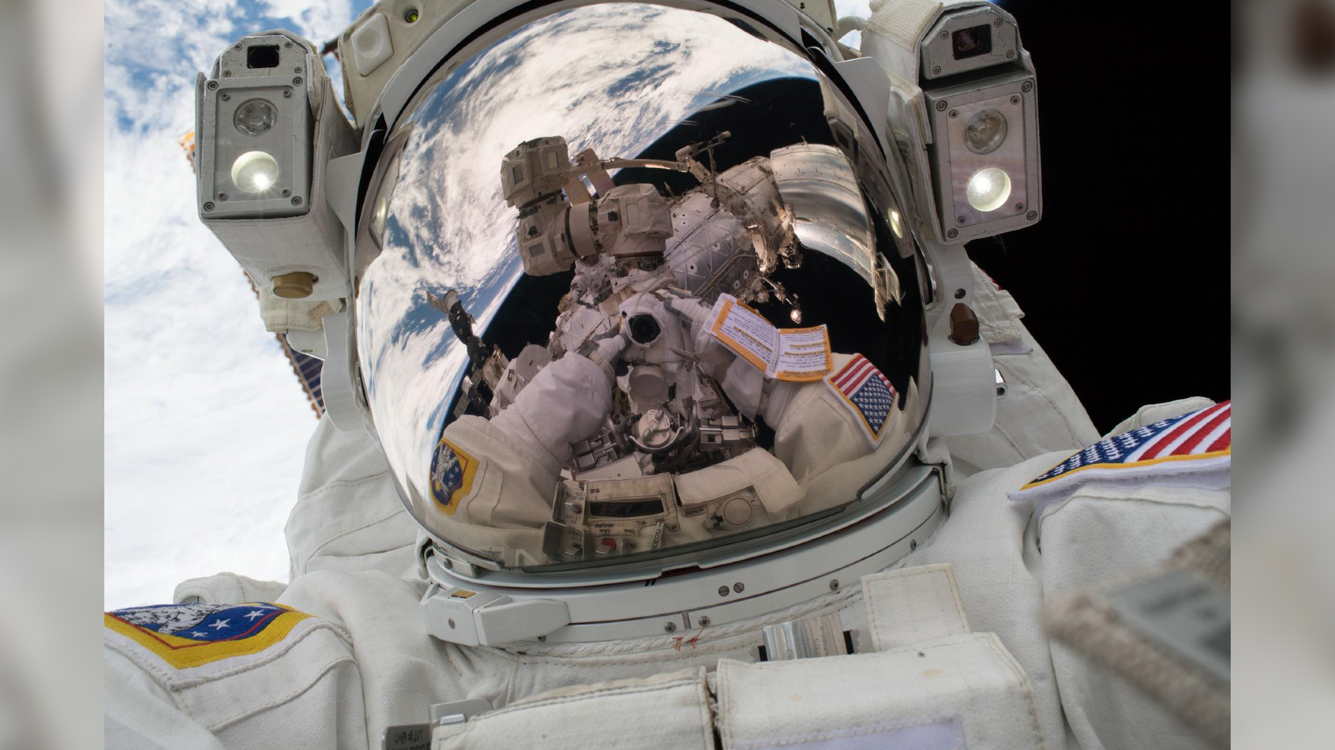 Close up of astronaut visor reflecting Earth in the background and the camera being used to capture the selfie.
