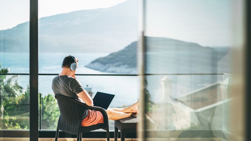 A young CEO and entrepreneur working from a remote seaside villa, sitting with a laptop outdoors on the balcony, using wireless headphones. Workation lifestyle, work and life balance.