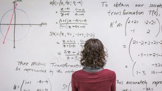 A woman stands in front of a whiteboard full of mathematics equations