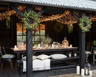 A covered seating area painted black with lights and wreath decorations
