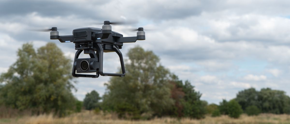 A picture of the Bwine F7GB2 drone in flight in a cloudy day with trees and clouds behind