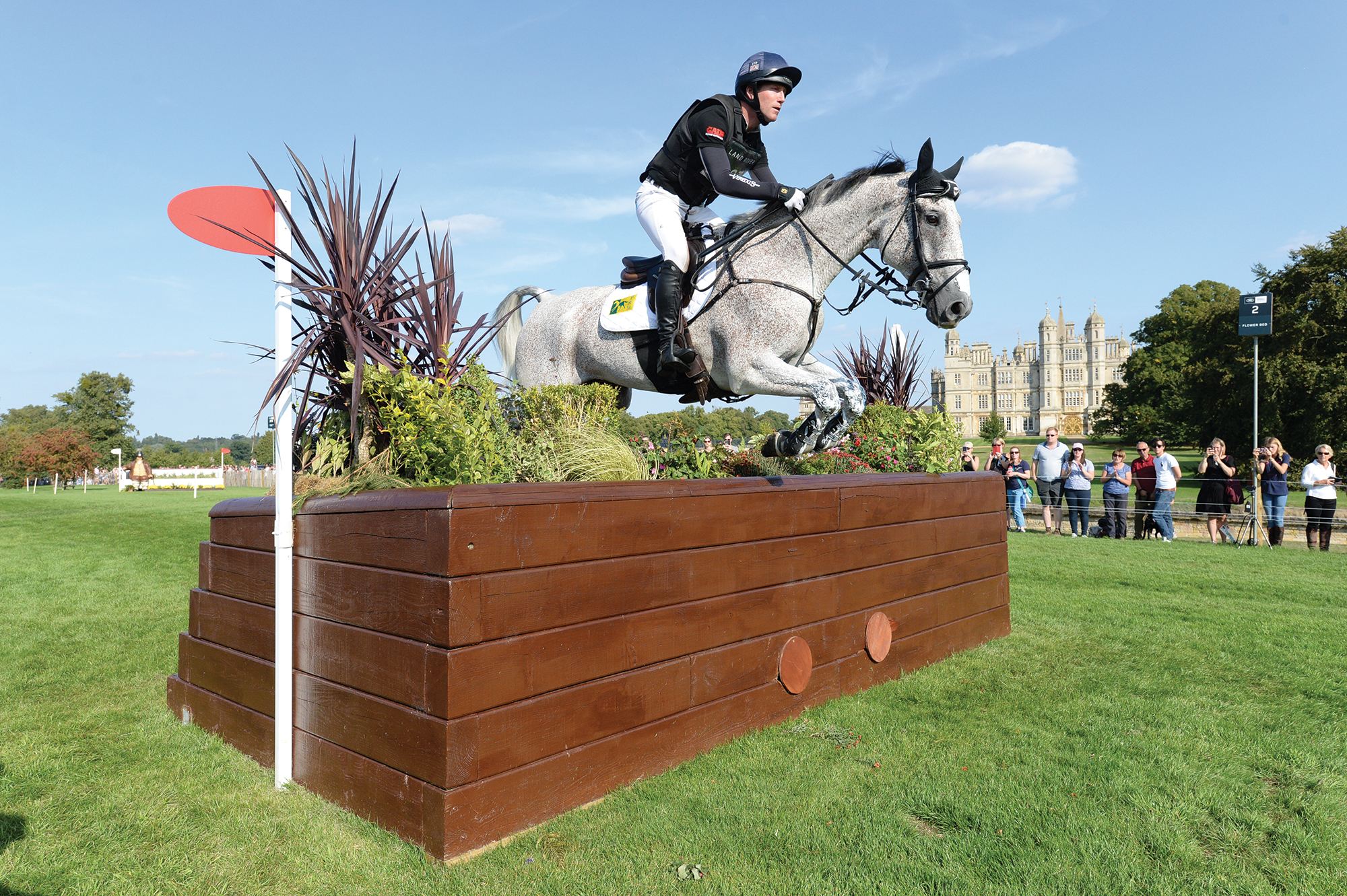 Oliver Townend and Ballaghmor Class clear a cross-country box fence in 2018 with Burghley House in the background.