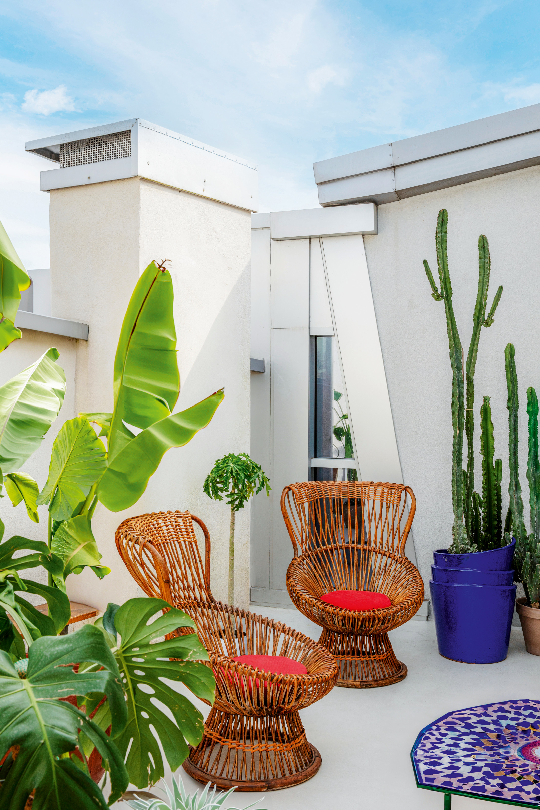 Balcony area with rattan chairs and blue and pink geometric tiled coffee table