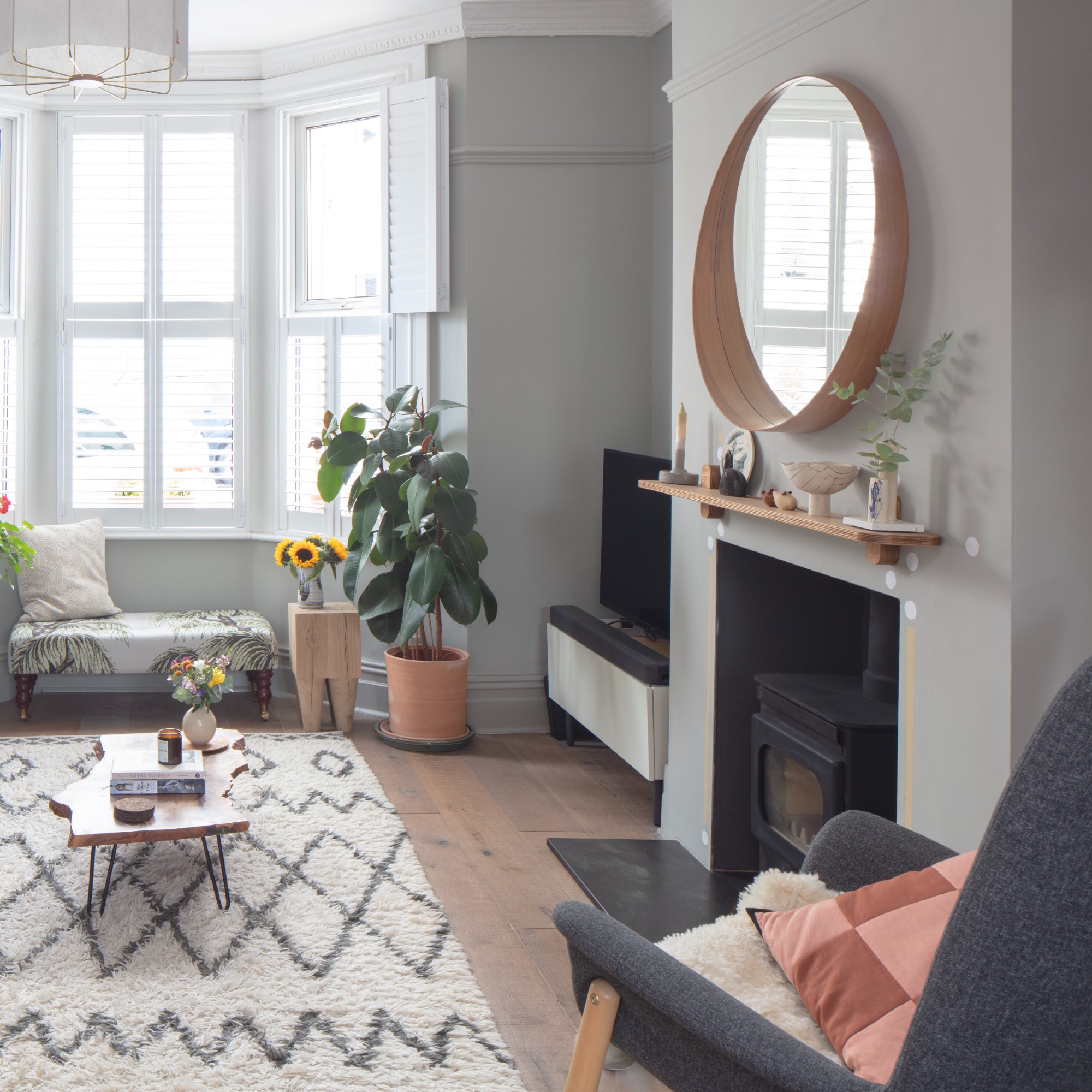 A grey living room with a Berber rug, a wood-burning stove and a round mirror above