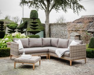 A rattan-effect outdoor corner sofa in a formal courtyard garden with topiary trees
