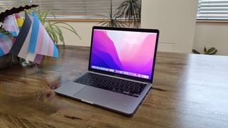 MacBook Pro 13-inch (M2, 2022) on a wooden table with trans pride flags in the background