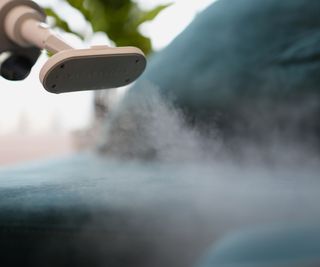 Someone using a steam cleaner on dark blue couch cushions