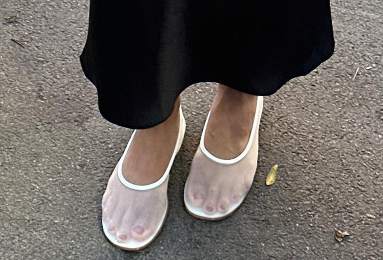 Close-up photo of woman wearing white mesh flats with black skirt.