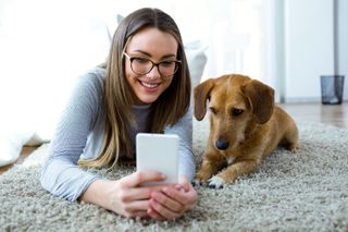 Woman and dog sitting on a rug looking at a smartphone