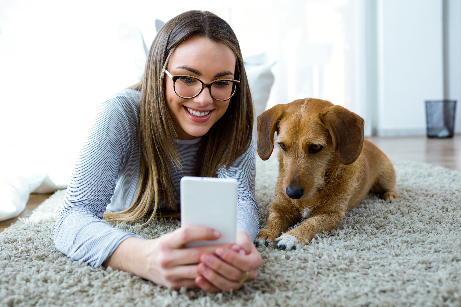 Woman and dog sitting on a rug looking at a smartphone