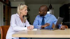 A woman sits with a male financial adviser with paperwork and an open laptop in front of them.