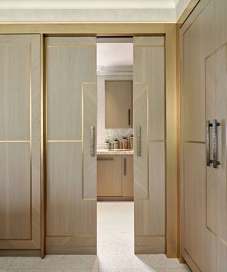 sliding pale wooden doors with gold detailing leading into walk in pantry