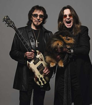 Tony Iommi with a guitar standing next to Ozzy Osbourne holding a dog