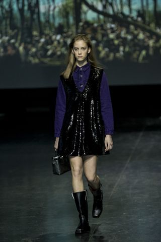 a model on the ganni runway wearing a black sequin dress with a pair of Ganni moto boots