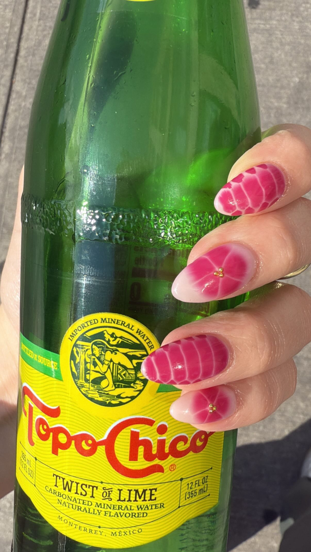 a hand with pink polish in a floral and snake skin design holding a green and yellow topo chico bottle