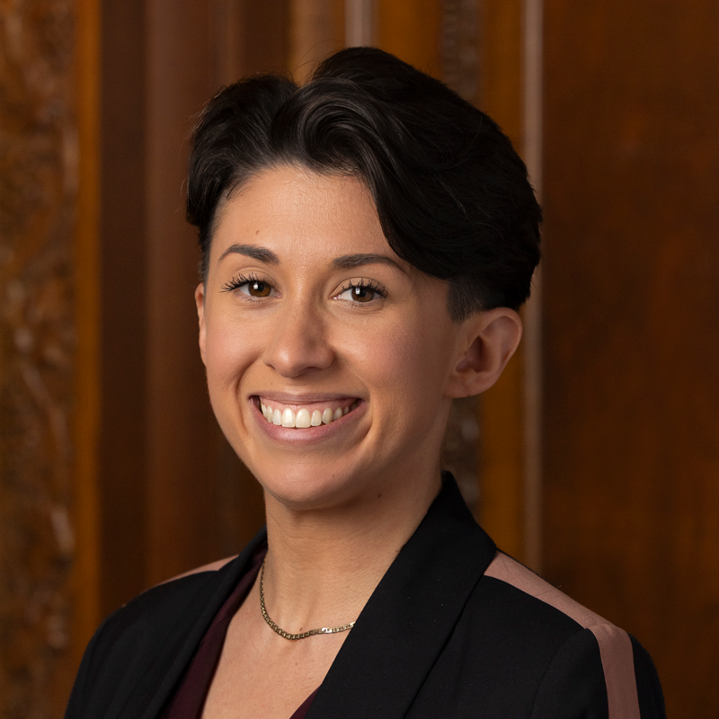 A woman with short hair wearing a dark jacket and gold necklace smiles at the camera.