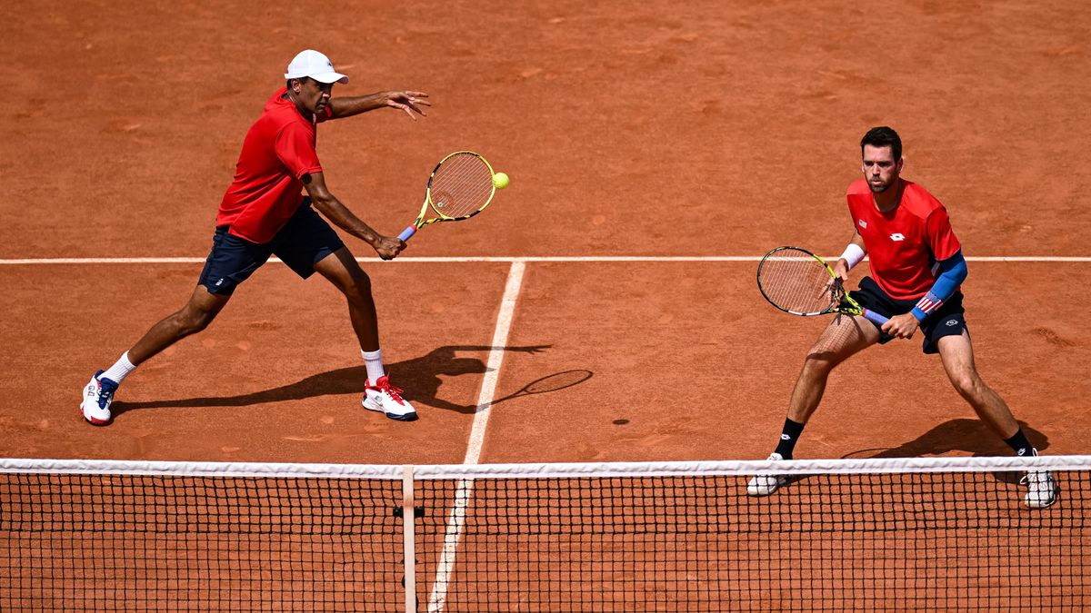 Rjeev Ram (L) and partner Austin Krajicek in red shirts and navy shorts playing in the men&#039;s doubles at the 2024 Olympic Games.