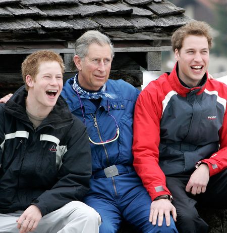 Prince William, Prince Harry and King Charles sitting next to each other wearing ski outfits and laughing