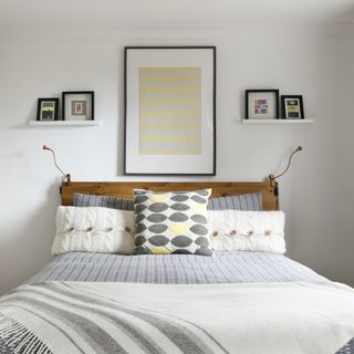 White bedroom with lights either side of bed and two small picture ledges