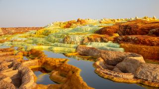 hot springs surrounded by orange and yellow mineral deposit formations.