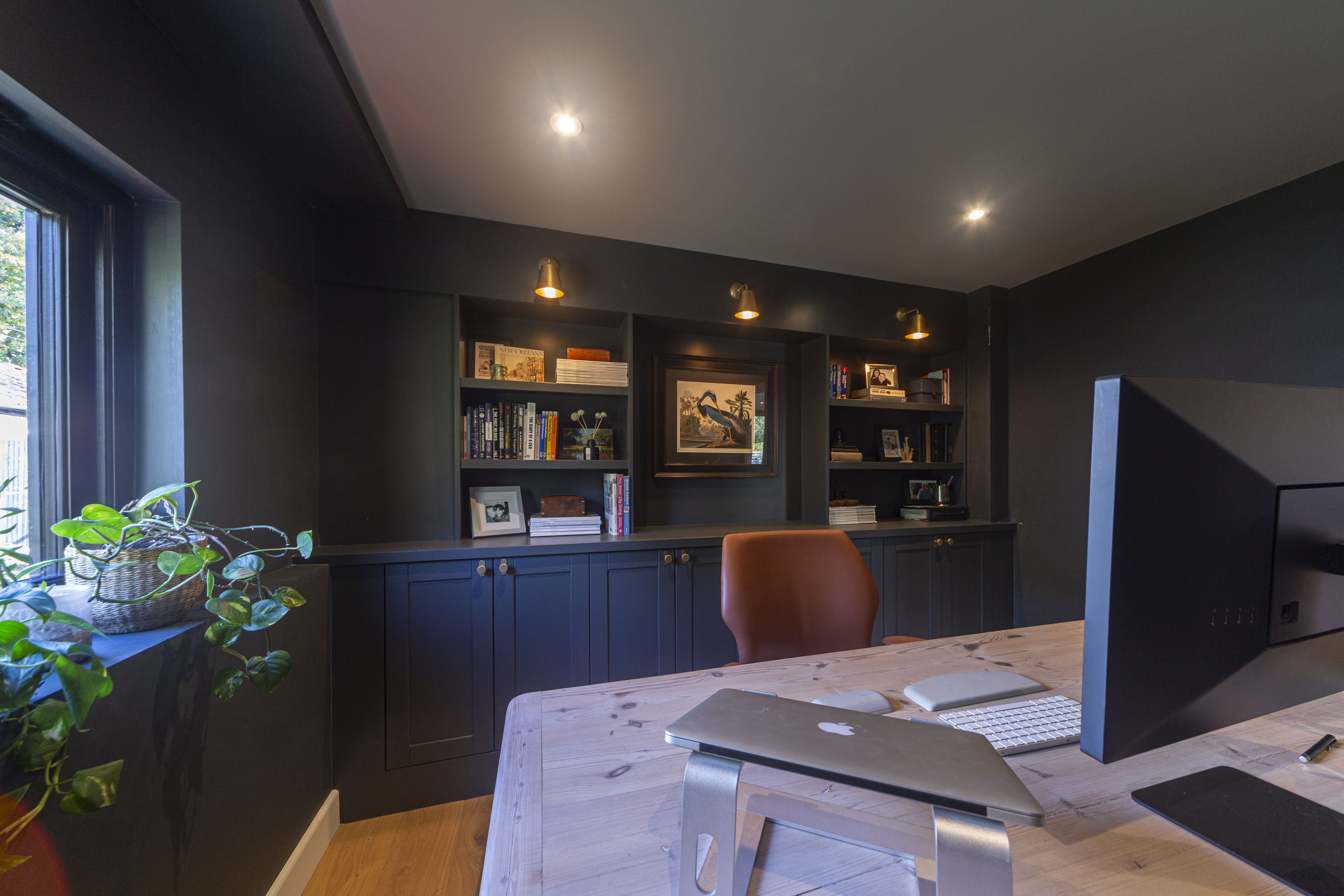 A dark office with a wall bookshelf with a wooden table with laptop and computer on it