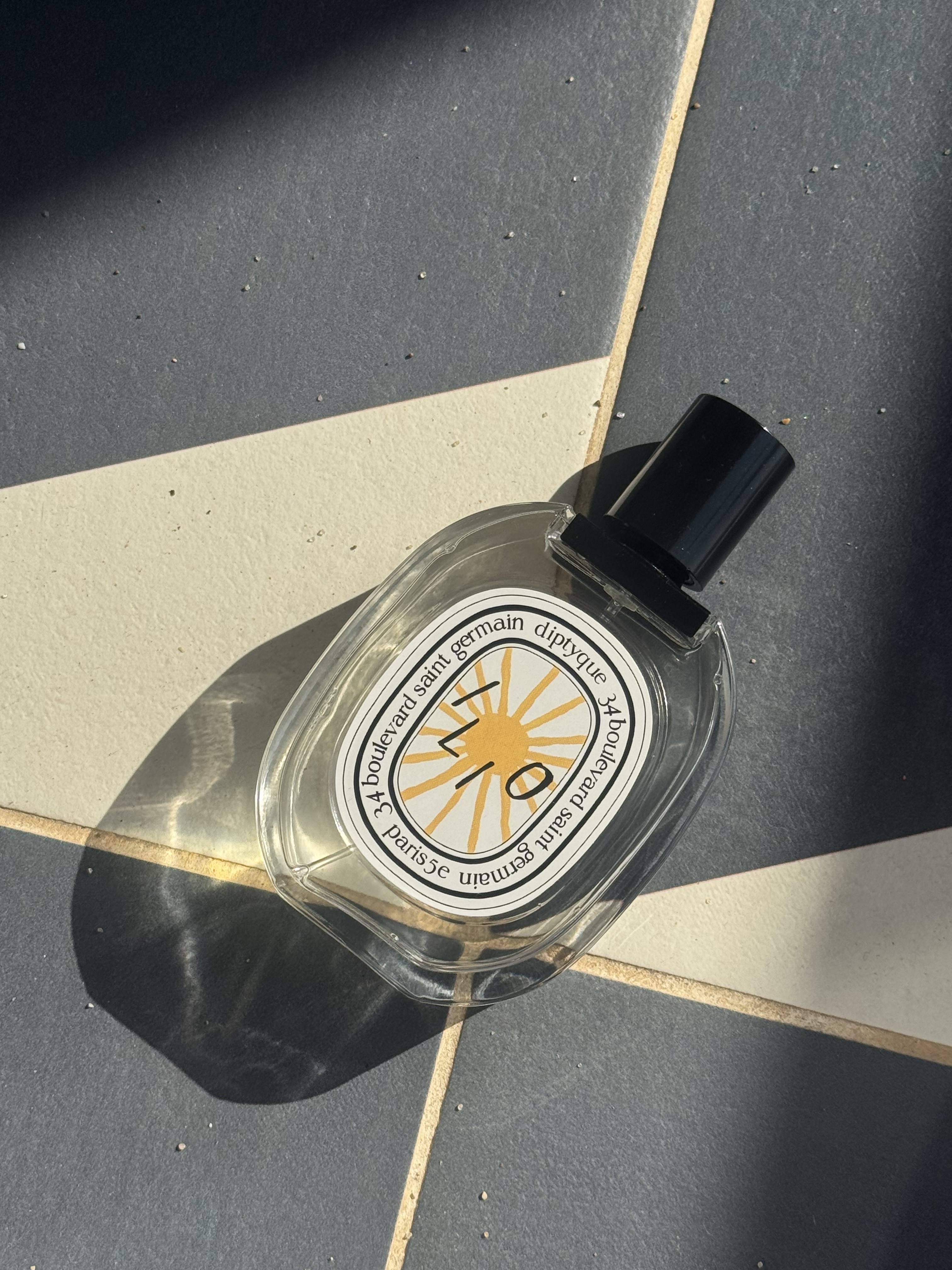 A bottle of Diptyque Ilio eau de toilette on a blue and white tiled background