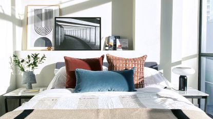 An apartment bedroom ideas example with scatter cushions in red ochre and teal, and artwork leaning on a shelf