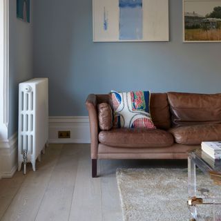 Blue living room with a brown leather sofa and a cream rug on wooden flooring with a white radiator on the wall on the left