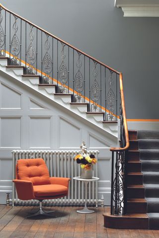 hallway with gray and white walls, staircase, orange accents, wooden floor, orange armchair, side table