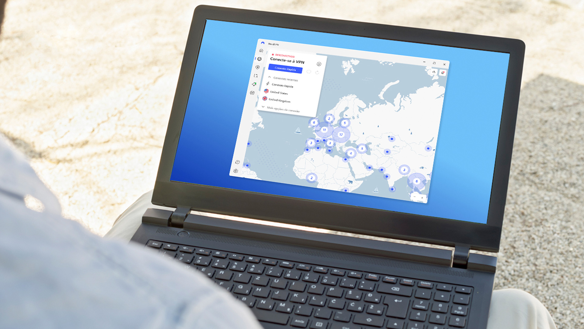 Someone sat at a beach uses a laptop displaying a NordVPN map