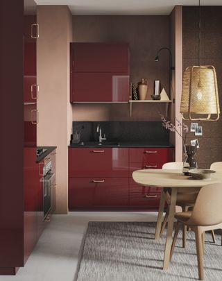 A small red kitchen with glossy cabinets, muted pink and brown walls and pale wood furnishings.