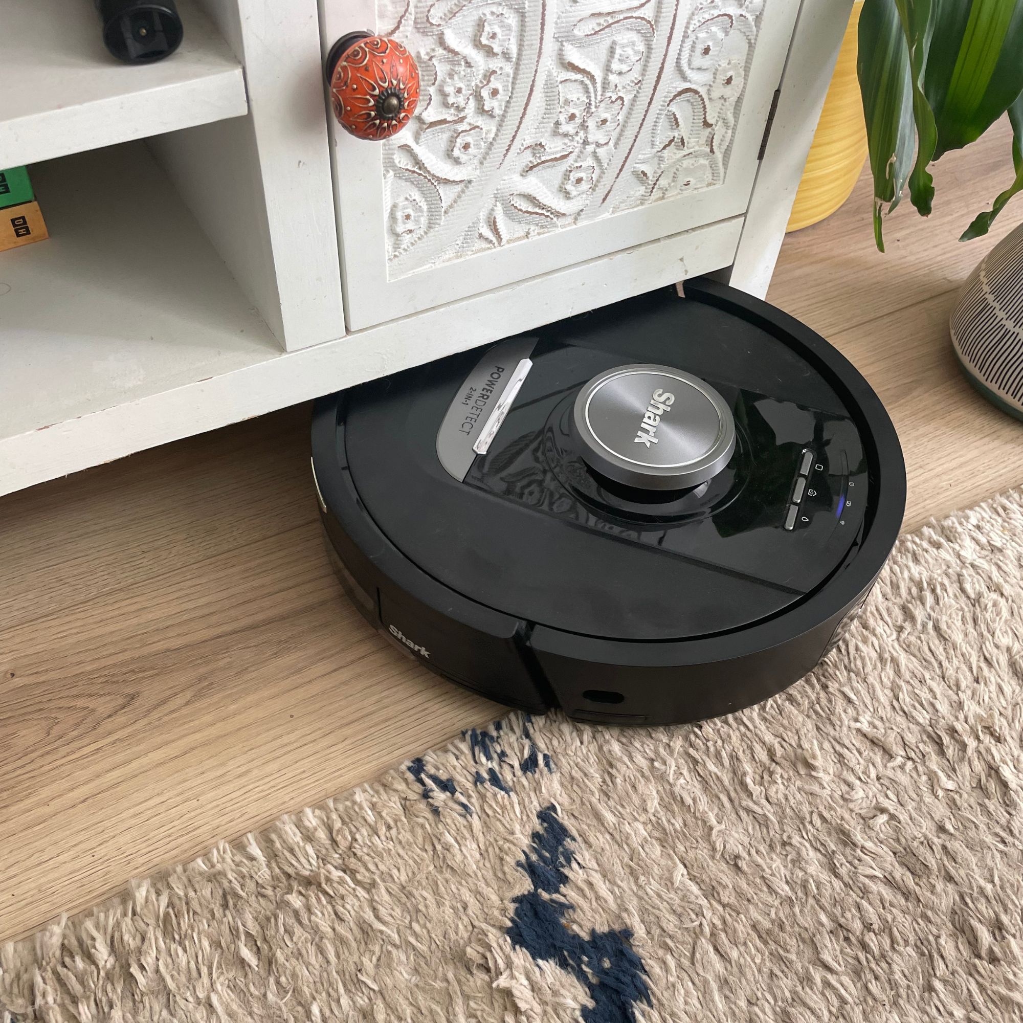Shark PowerDetect NeverTouch Robot Vacuum and Mop hitting the bottom of a white TV unit