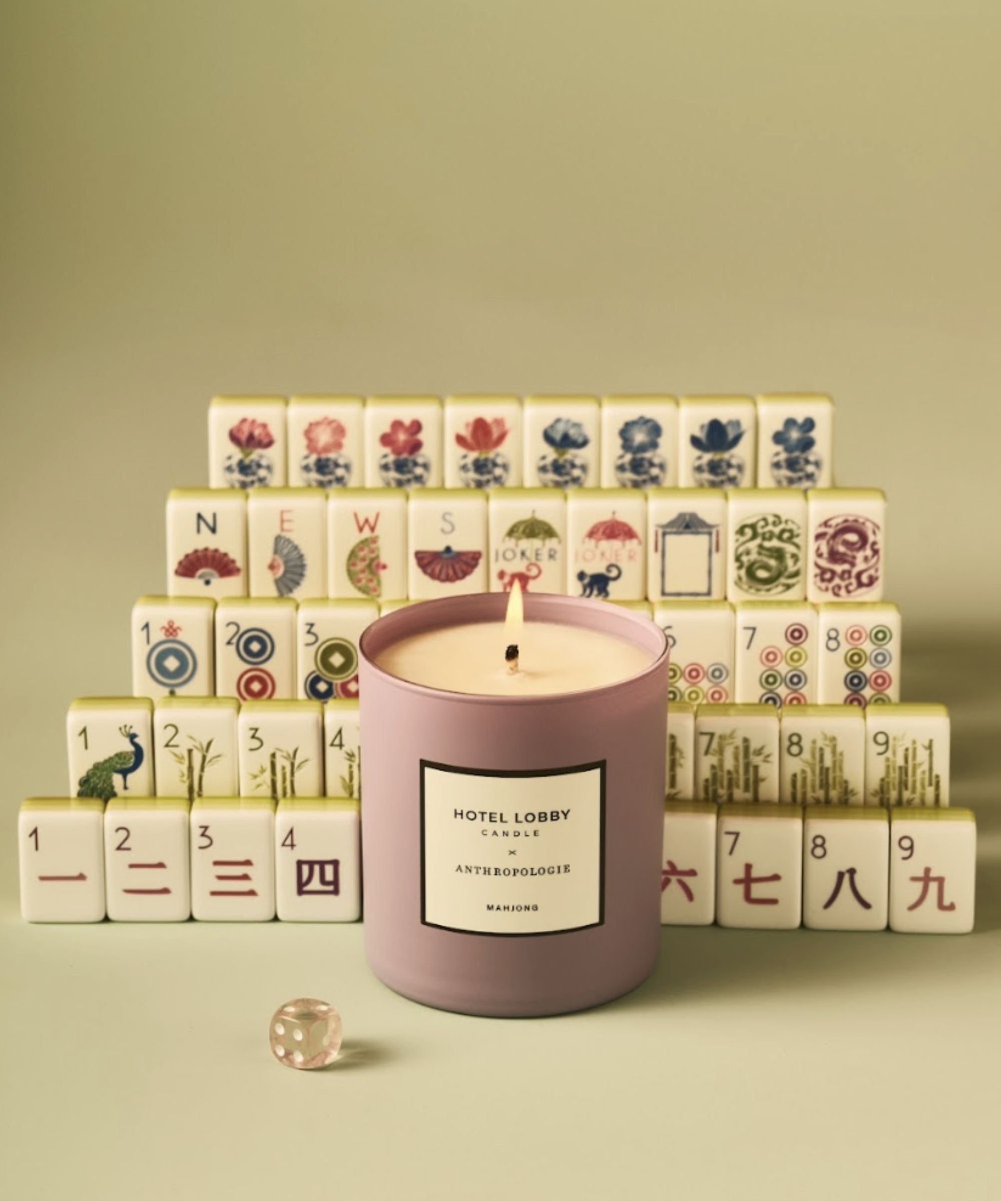 The purple Hotel Lobby Mahjong candle lit, against a tower of colorful and decorative Mahjong tiles and a pale green background, with a clear purple dice in the foreground.