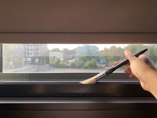 A paintbrush being used to dust a window track