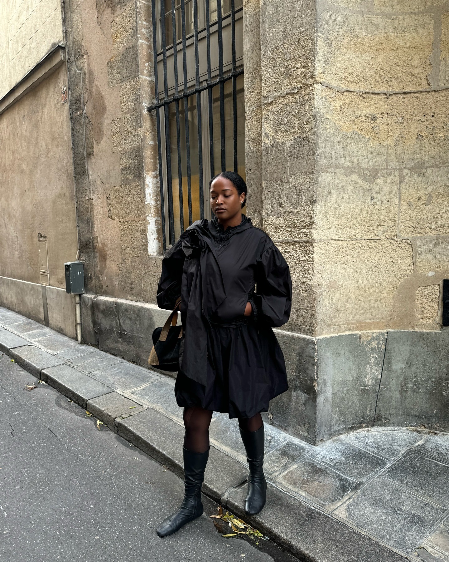A woman wearing an all black long sleeve top, and black short skirt, and black leather boots