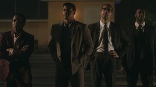 A still from the movie One Night in Miami showing the four main characters Malcolm X (Kingsley Ben-Adir), Muhammad Ali (Eli Goree), Jim Brown (Aldis Hodge), and Sam Cooke (Leslie Odom Jr) stood outside in the dark and wearing suits.