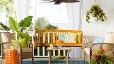 Colorful front porch ideas by Wayfair with orange side table, wooden bench and rattan seating
