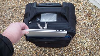 Laptop being pulled out of a Think Tank Airport International V3.0 travel case on a gravel surface