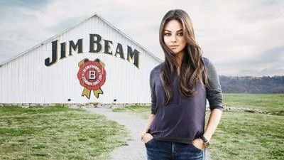 Mila Kunis posing on gravel path, in front of Jim Bean barn