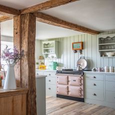 country kitchen with tongue and groove splashback, pink range cooker, green cabinets, wooden beams