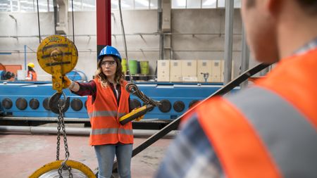 A woman wearing a blue hardhat operates a crane on a job site.
