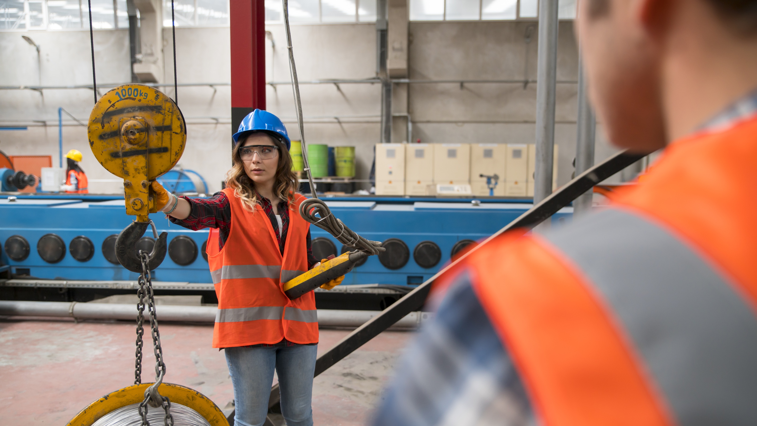 A woman wearing a blue hardhat operates a crane on a job site.